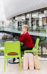 Portrait of an elderly woman sitting at a table in a shopping mall.