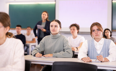 Female college students sit at desk and write in textbook