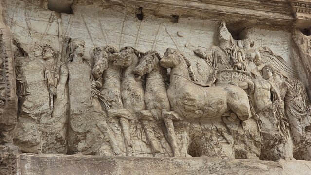 Rome, Italy - 13 January 2025. A relief on the Arch of Titus shows Emperor Titus in a chariot drawn by four horses, surrounded by attendants and a winged figure crowning him with victory.