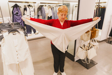 An elderly woman measures the length of her trousers with her hands in a store.