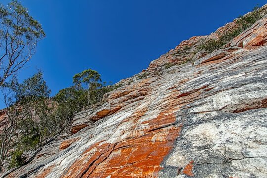 Close-up of a rocky cliff face, with vibrant colors and trees at the bottom