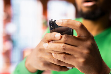 Focus on smartphone used by african american man playing videogames, enjoying leisure time at home. Close up of gamer enjoying game on mobile phone, having fun in apartment