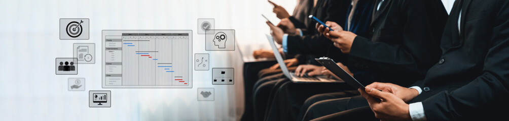 Group of professionals engaged in project management tasks using mobile devices and laptops,...