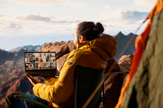 Entrepreneur uses high speed internet connection on mountain top, enjoying the video call with a scenic landscape. Young hiker having an internet dependency and being workaholic.