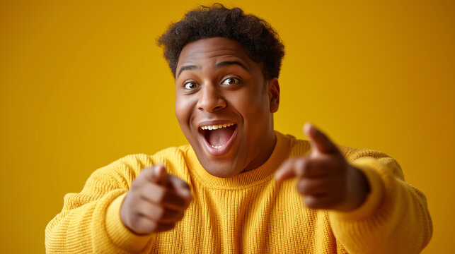 An excited young man from a diverse background pointing sideways against a vibrant yellow background, diversity, inclusivity, interracial couples, plus-size models, energetic portr