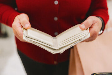 An elderly woman in a red sweater looks at a white money purse.