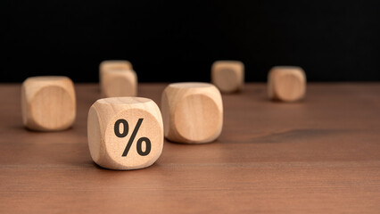 wooden cube with black percent sign on brown wooden table with blurred cubes and dark background