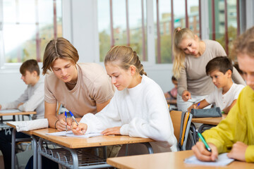 Teen boys and girls sitting at desk in classroom full of pupils during lesson