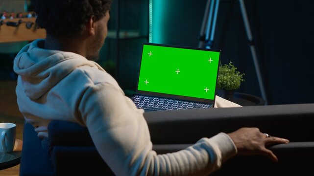 Happy pleased young man employs isolated copy space at home, relaxing on his couch in a modern living room decorated with neon lights and trendy furniture. Male person with gadgets. Camera A. - Powered by Adobe