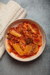 Kimchi, a fermented napa cabbage Korean dish, in a rustic ceramic bowl on a grey concrete background with a linen napkin, capturing its vibrant color and texture from a top down view