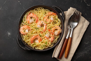 Shrimps pasta spaghetti served in a black cast iron skillet garnished with fresh lemon slices and parsley top view on black rustic background