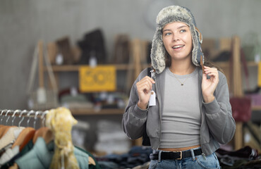 Fototapeta premium Positive young girl trying on fur hat while shopping in clothing store