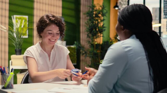 Interviewer handing workplace entrance card to black man after the hiring decision, completing identification with ID confirmation on badge for the role within corporate office system. Camera B.