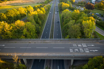 An overhead aerial view of a motorway overpass, showing traffic flowing on the bridge and the dual carriageway below, with prominent road markings indicating directions and place names.