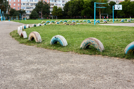 Explore a captivating outdoor sports field, adorned with vintage car tires and basketball hoops, capturing a unique blend of urban landscapes, children's playgrounds, and street scenes on an overcast