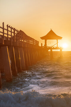 Waves crash against the Naples Beach Pier at Golden Hour Sunset, Florida, USA
