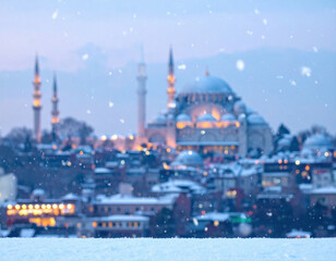 Fototapeta premium Snow falling over Istanbul cityscape with mosque and minarets illuminated in the winter evening.