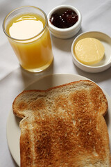 Breakfast setup presenting plain toasted bread, orange juice, strawberry jam, and butter. Cotswolds countryside, England