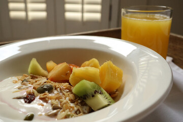 Breakfast bowl offering healthy yogurt, granola, and sliced fruits with orange juice. Cotswolds countryside, England