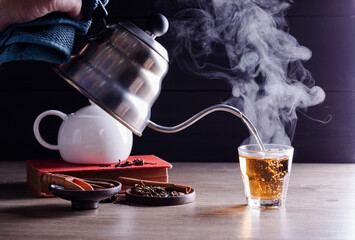 Pour hot tea into cups, herbal tea glasses are arranged on a rustic wooden table.