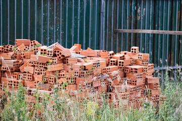 Stack of orange-red bricks stored together near green construction fencing