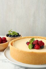 Delicious cheesecake with fresh berries and mint on white marble table, closeup