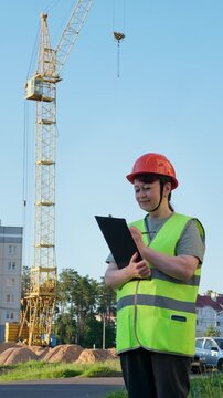 A female engineer in uniform and hard hat inspects construction. A crane is in the background. 4K video