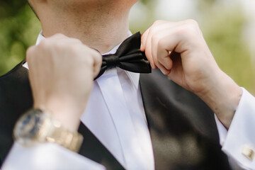 Close-up of man tying elegant bow tie to white shirt collar, detail of hands adjusting formal accessory
