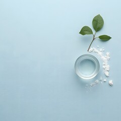 Top view of glass water cup with ice cubes and green leaves on light blue background, symbolizing freshness, hydration, purity, and clean natural wellness concept for health, spa, and eco-friendly des