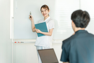 Fototapeta premium Female staff including nurses, pharmacists, and registered dietitians explaining in front of a whiteboard at a medical conference 