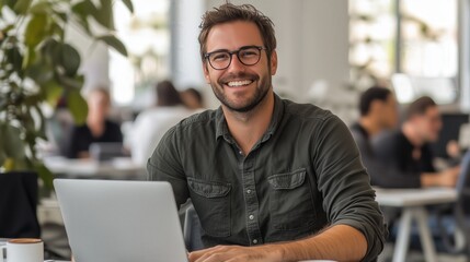 A casual young man smiles while working on his laptop at a table, enjoying coffee and productivity.