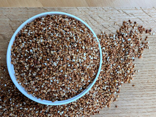 Raw buckwheat in a white bowl on the wooden kitchen board. Top view