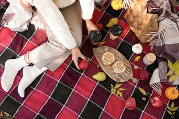 Young woman with cups of coffee, fruits and buns sitting on picnic in autumn park, top view