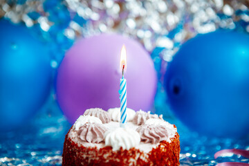 Happy birthday cake with burning one candle and blue and purple air balloons on silver background