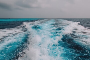 A boat's wake streaks across the ocean's surface, leading towards the horizon under a cloudy sky