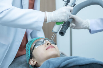 Asian woman wearing protection glasses getting laser skin face treatment.