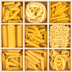 Various pasta shapes, including penne, rigatoni, fusilli, and fettuccine, are arranged in a wooden box, providing a visually appealing presentation of different culinary options.