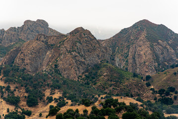 Obraz premium A close shot of the gray, rocky mountain peaks and green trees and grass in the foothills at Malibu Creek State Park in Calabasas, California in the Santa Monica Mountains. 