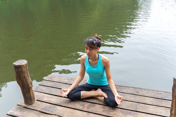 Young woman yoga teacher performs carry out exercises in solitude outdoors, in shady city park alone. She does exercises and repeats lotus position, padmasana