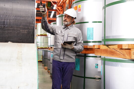 elderly engineer is inspecting the inventory of rolled steel and controlling the operation of machinery in a factory.