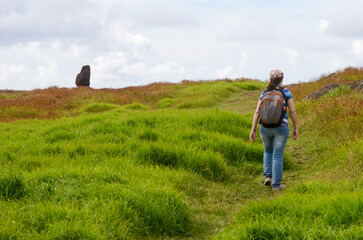 Woman hiking towards statue in lush grass under cloudy sky