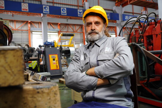 An experienced senior male steel cutter wearing a safety helmet works in a factory, take a break to check the quality of the steel cut in a metal roofing factory. - Powered by Adobe