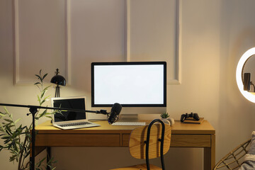 Blogger's workplace with computers, lamp and microphone in evening office