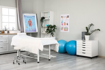 Interior of massage therapist's office with couch, fitness balls and poster on flipchart in modern...