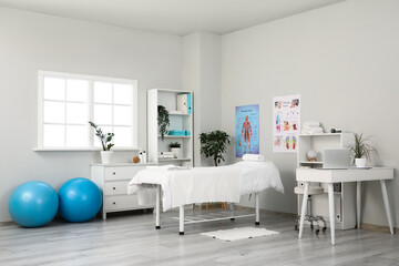 Interior of massage therapist's office with workplace, couch, fitness balls and posters on wall in...
