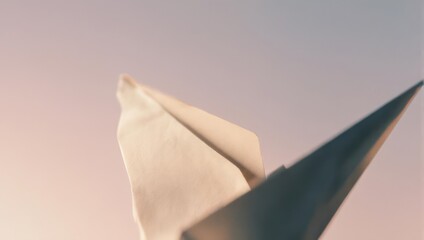 Close-up of a folded paper airplane against a soft, pastel sky.  The plane's design is intricate, showing folds.  Gentle, diffused light emphasizes the paper's texture