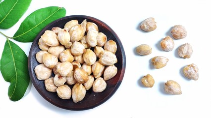 Top view of Candlenut seed or biji kemiri (Aleurites moluccanus) in clay plate. Isolated on white background with copy space. Suitable for design element, food article, or health concept.