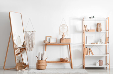 Interior of living room with mirror, wooden bench and different home decor in shelving unit