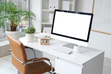 Stylish workplace with modern computer, cube calendar and cup of coffee in light office