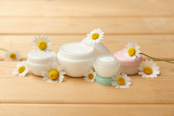 Jars of chamomile cosmetic cream and flowers on wooden background